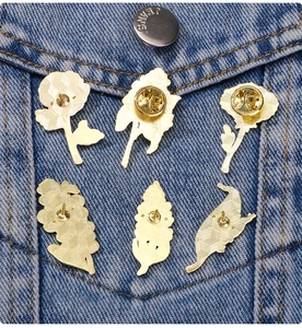 Detail of six floral enamel pins with gold metal finish pinned on a blue denim jacket pocket