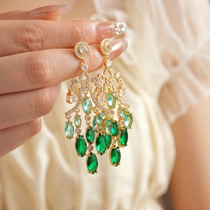Close-up of gold dangle earrings with gradient green stones and sparkling zircon details