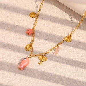 18K gold plated paperclip necklace with pink shell fish and sea charms over textured background