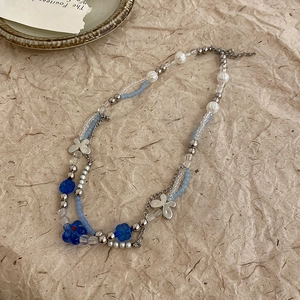 Detail of beaded necklace featuring blue flowers and irregular geometric silver pendants