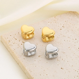 Macro detail of gold and silver heart-shaped hoop earrings with a mirror-polished finish