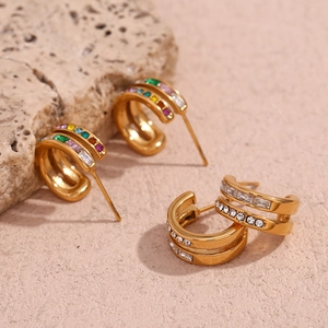 Detail view of gold double C-shaped earrings with colorful zirconia inlay on stone background