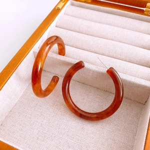 Close-up of C-shaped tortoiseshell resin hoop earrings in a wooden jewelry box