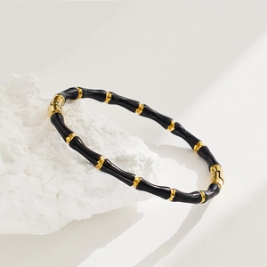 Bamboo style bangle in black enamel and gold finish on a minimalist stone display