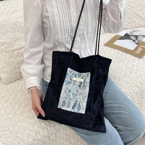 Détail du sac cabas en velours noir avec broderie de dentelle bleue porté par un modèle