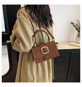 Borsa a mano retrò marrone in pelle con fibbia dorata indossata da modella in cappotto beige