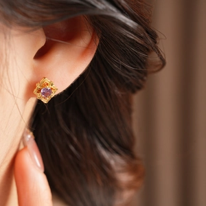 Detailed close-up of a vintage gold floral earring with a purple gemstone on an ear lobe