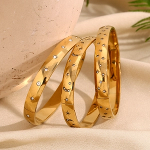 Detail of 18K gold plated bangles with star, moon, and evil eye charms with white diamonds