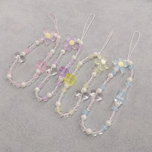 Detail of four colorful beaded phone straps with heart and flower charms on grey fabric