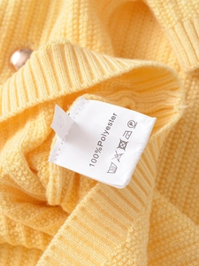 Detail of care label on yellow polyester cardigan showing size and washing symbols