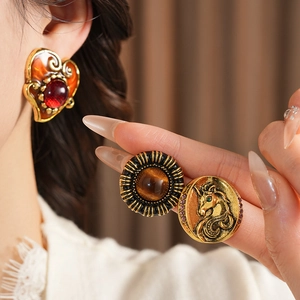 Macro shot of vintage gold earrings with red resin heart and amber gemstone details