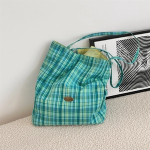Close-up of the metal logo on a green and blue plaid canvas tote bag in a cozy setting