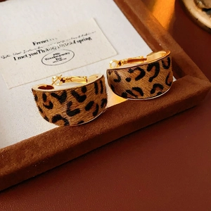 Macro shot of gold-plated leopard print hoop earrings on a velvet display tray