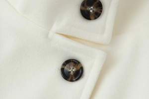 Detailed macro shot of white wool coat featuring brown tortoiseshell pattern buttons