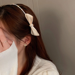 Detail of cream fabric bow headband with rhinestone accents on a female model