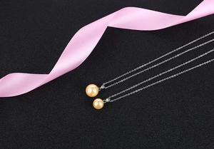 Detail of two champagne gold pearl pendants on silver chains over a dark background