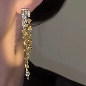 Detail of long tassel earrings featuring golden metal discs and sparkling zircons