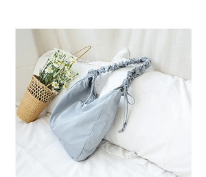 Close-up of light blue pleated cloud bag on white bedding with decorative flower basket