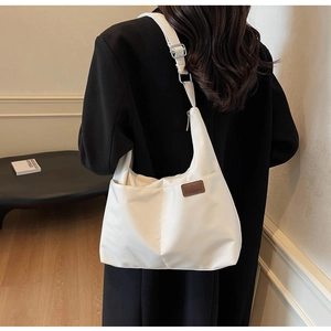 Detailed view of a white canvas tote bag with a brown leather logo patch on a black coat