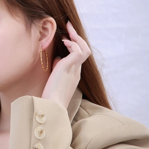 Close-up of golden bamboo textured hoop earring worn by a model in a beige blazer
