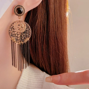Close-up of vintage gold tassel earrings with coin charms and black inlay on a model