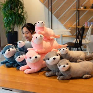 Three colorful otter plush toys in pink, gray and navy blue displayed on a wooden desk