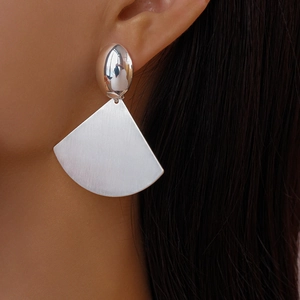Close-up of geometric fan-shaped silver drop earrings with brushed metal texture finish