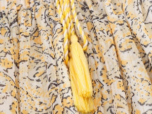 Detail of yellow floral print fabric with woven tassel tie and gold metallic thread accents