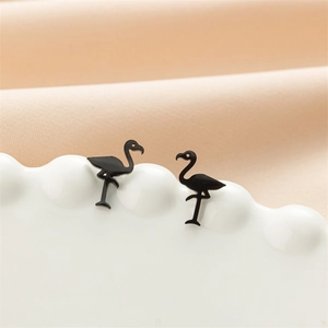 Macro shot of black flamingo stud earrings on a white wavy ceramic display stand
