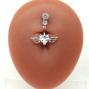 Macro shot of silver heart belly button ring with wings and zircon stones on a model