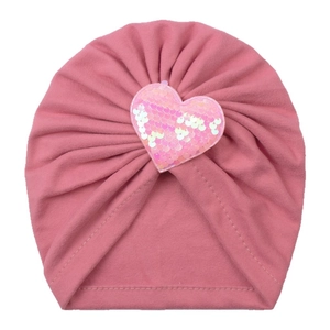 Détail du bonnet rose tricoté pour bébé avec cœur en paillettes et texture plissée