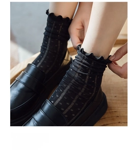 Detail of sheer black lace crew socks with polka dots and ruffled edges on loafers