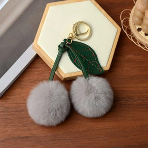 Close-up of grey faux rabbit fur cherry keychain with green leather leaves and gold clasp