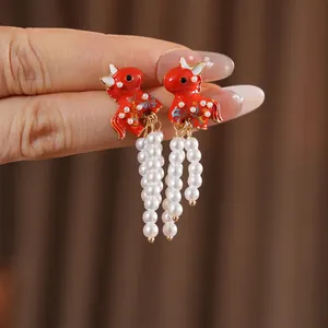 Vintage enamel auspicious beast earrings with white pearl tassels on a warm fabric background