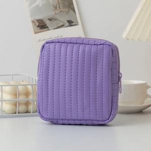 Close-up of quilted purple leather cosmetic pouch with zipper on a minimalist white table