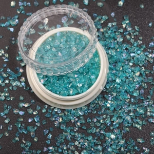 Macro shot of sparkling blue-green iridescent glass glitter flakes in a round container