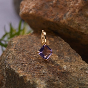 Detail of square-cut purple gemstone pendant in gold finish on a natural rock texture
