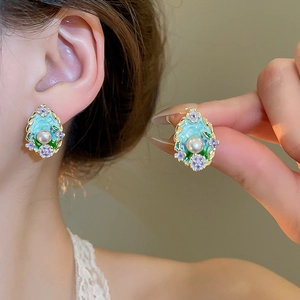 Close-up of mint green enamel flower earrings with pearl accents and gold metal trim