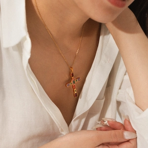Close-up of gold cross necklace with multicolored gemstones worn by a model