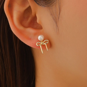 Detail of elegant gold bow earrings with a white pearl on a model's ear lobe