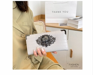 Detail of grey crocodile texture clutch with ornate metal skull and floral carving