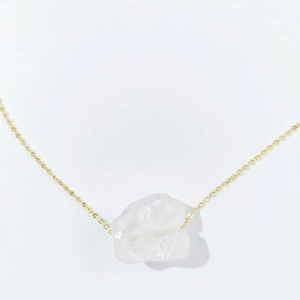 Close-up of raw white crystal stone pendant on a delicate gold chain necklace