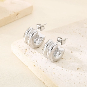 Gros plan de boucles d'oreilles C argentées épaisses avec rainures sur pierre beige