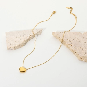 Close-up of golden heart pendant on a snake chain over minimalist stone blocks