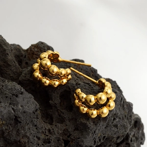 Double-row golden bead C-shape earrings displayed on rustic volcanic stone