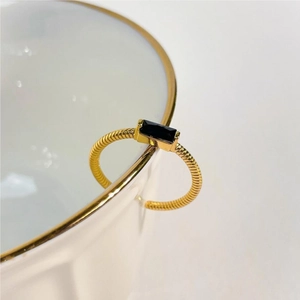 Detail of gold spiral ring with black rectangular zircon stone on a white ceramic rim