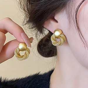 Detailed view of matte gold woven chain hoop earrings worn and held by a model