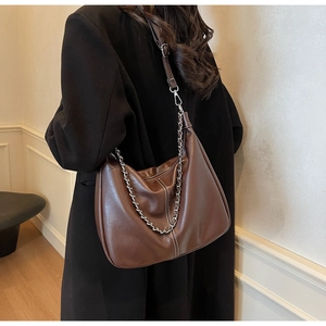 Close-up of brown leather hobo bag with silver chain detail on a black coat