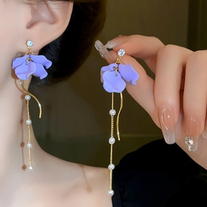Détail de boucles d'oreilles pétales mauves avec glands dorés et perles sur un modèle