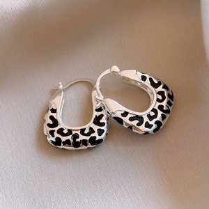 Macro detail of U-shaped silver hoop earrings with black leopard print on beige silk